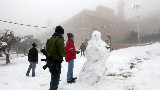 Verschneite Landschaft mit einem Schneemann und mehreren Personen im Hintergrund.