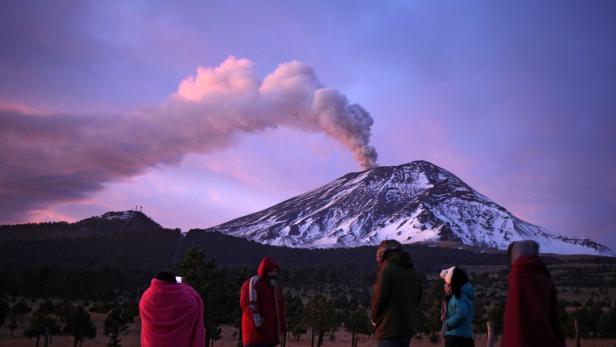 Menschen beobachten den rauchenden Vulkan Popocatépetl bei Sonnenaufgang.
