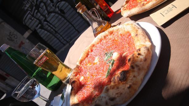 Eine Pizza mit Tomatensauce und Basilikum auf einem Tisch mit Getränken.