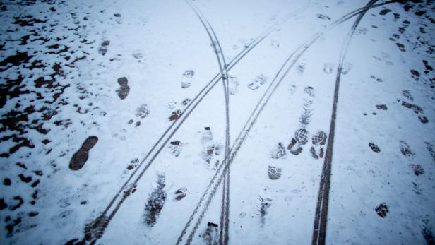 Schneebedeckter Boden mit Fußspuren und Reifenspuren.