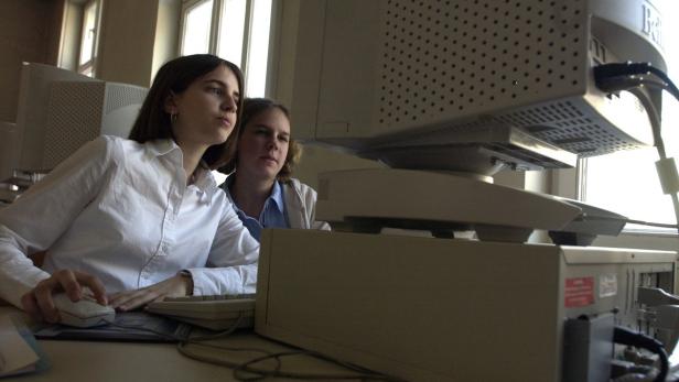 Zwei junge Frauen arbeiten an einem alten Computer mit Röhrenmonitor.