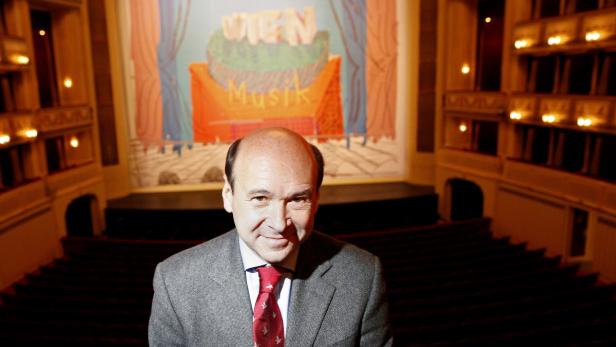 Ein Mann im Anzug steht vor der Bühne eines Theaters mit dem Schriftzug „Wien Musik“.