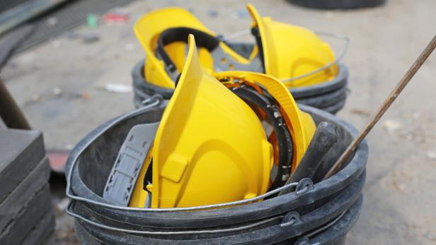 Gelbe Bauhelme liegen in schwarzen Eimern.