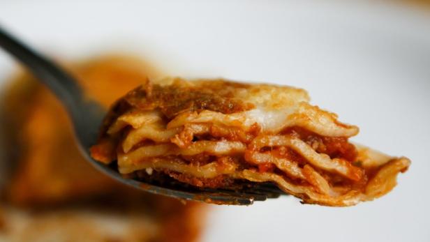 Ein Stück Lasagne mit Tomatensauce auf einer Gabel.