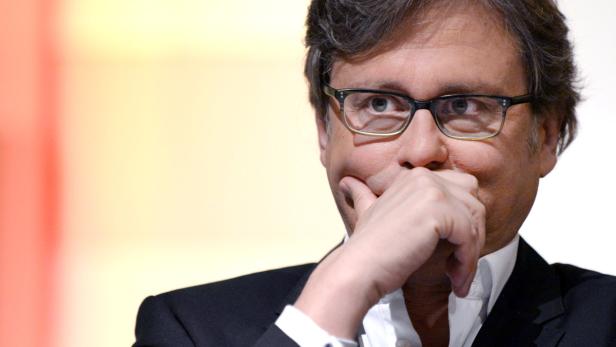 Ein Mann mit Brille und Anzug hält seine Hand vor das Gesicht.