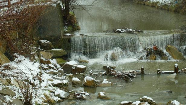 Ein kleiner Wasserfall in einem Bach, umgeben von schneebedeckten Steinen.