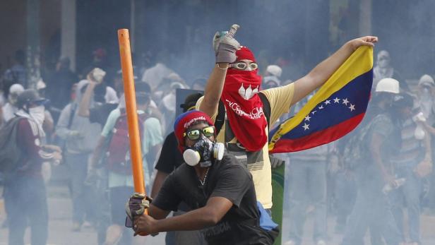 Demonstranten mit venezolanischer Flagge und Schutzmasken inmitten von Rauch.