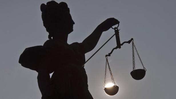 Die Silhouette der Justitia mit einer Waage vor einem hellen Hintergrund.