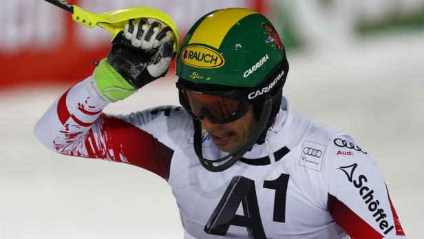 Ein Skirennläufer mit Helm und Skibrille hält einen Skistock in der Hand.