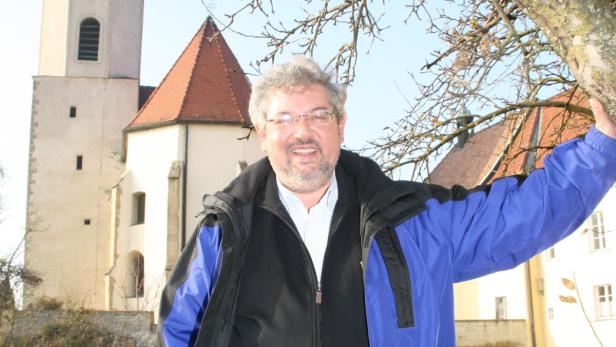 Ein Mann steht vor einer Kirche mit einem markanten Turm.