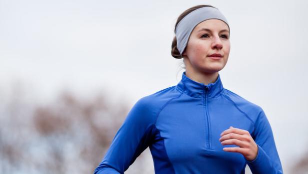 Eine Frau mit Stirnband und blauem Sportoberteil läuft.