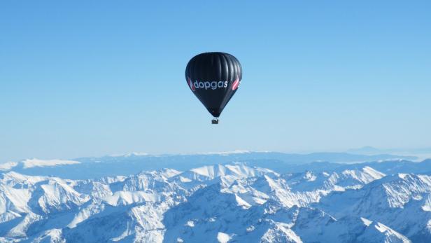 Ein „dopgas“-Heißluftballon fliegt über schneebedeckte Berge.