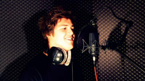 Ein junger Mann mit Kopfhörern spricht in einem Aufnahmestudio in ein Mikrofon.