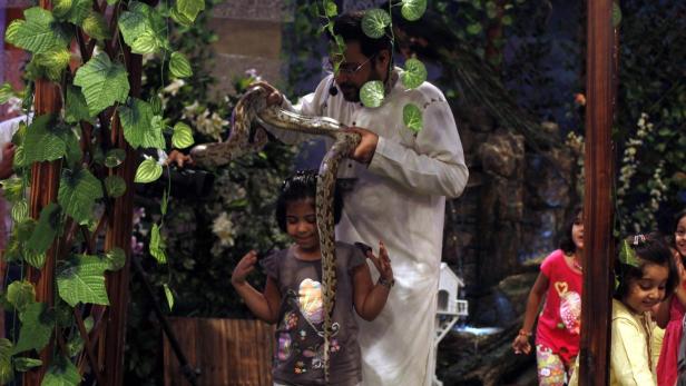 Aamir Liaquat Hussain, host of the Geo TV channel programme &quot;Amaan Ramazan&quot;, puts a snake around a child&#039;s shoulders during a live show in Karachi July 26, 2013. In a ruthless quest for ratings, Pakistani television is screening what many describe as its most controversial content yet: a talk-show host who gives away babies as prizes. Hussain gave away two abandoned infant girls to childless families last month and plans to give away a baby boy this week. The children in this picture are not the children being given away. Picture taken July 26, 2013. REUTERS/Akhtar Soomro (PAKISTAN Tags: ENTERTAINMENT SOCIETY)