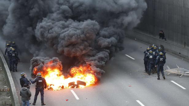 Auf einer Straße brennt ein Feuer, während Polizisten in der Nähe stehen.