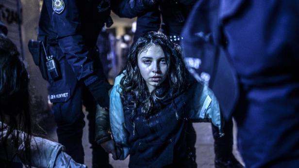 Eine junge Frau mit Tränen in den Augen wird von Polizisten abgeführt.