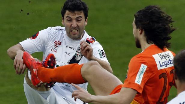 Ein Fußballspieler wird von einem anderen gefoult, wobei Dreck aufwirbelt.