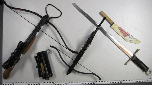 Eine Armbrust mit Zielfernrohr, eine kleine Armbrust, ein Schwert und ein Messer liegen auf einem Tisch.