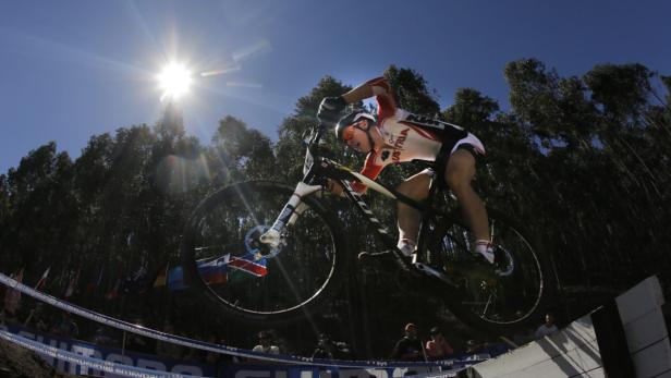 Ein Mountainbiker springt über eine Rampe vor einem Publikum und Flaggen.