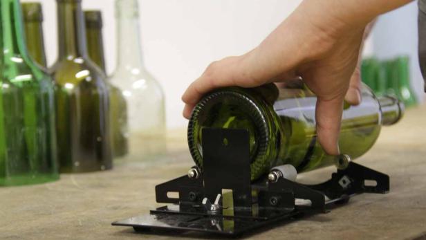 Eine grüne Glasflasche wird mit einem Glasschneider bearbeitet.