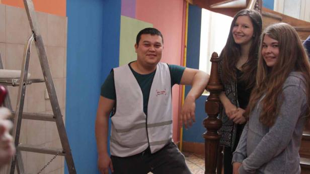 Ein Mann in Arbeitskleidung steht mit zwei jungen Frauen in einem Treppenhaus.