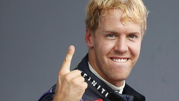 Sebastian Vettel zeigt mit dem Finger nach oben und lächelt.