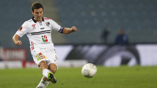 Ein Fußballspieler in weißem Trikot schießt einen Ball.