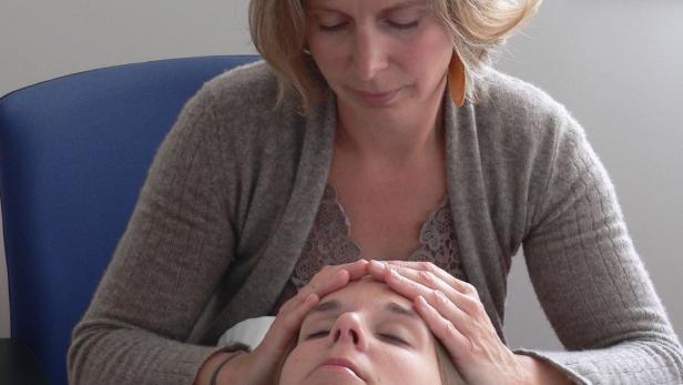 Eine Frau behandelt eine andere Frau, indem sie ihre Hände auf ihre Stirn legt.