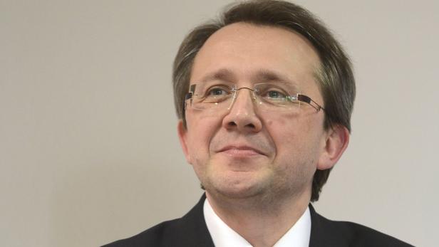 Ein Mann mit Brille und dunklem Anzug blickt lächelnd zur Seite.