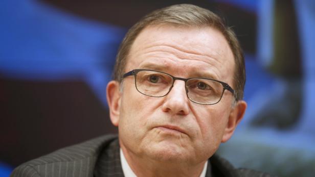 Ein Mann mit Brille und Anzug blickt ernst in die Kamera.