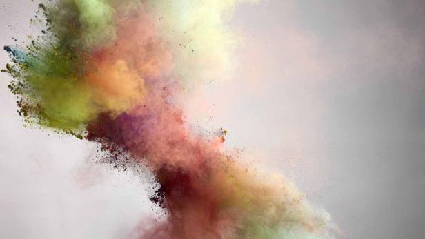 Eine Explosion aus buntem Farbpulver vor einem grauen Hintergrund.