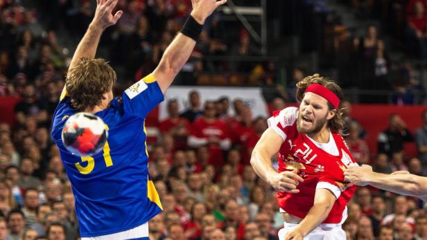 Ein Handballspieler im roten Trikot wird von einem Gegenspieler im blauen Trikot am Trikot gezogen.