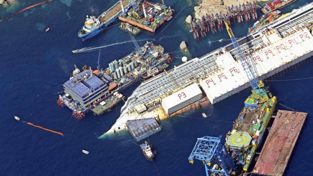 Das havarierte Kreuzfahrtschiff Costa Concordia liegt im Wasser, umgeben von Bergungsschiffen.