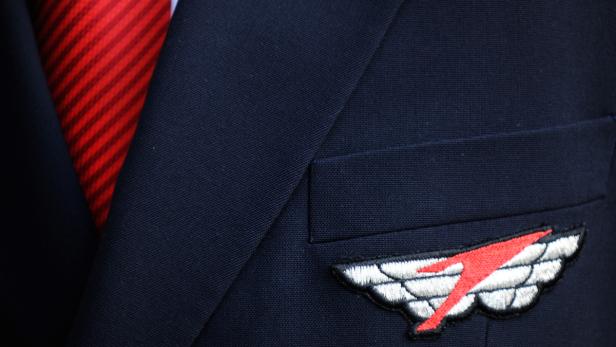 Nahaufnahme eines blauen Sakkos mit roter Krawatte und einem geflügelten Abzeichen.