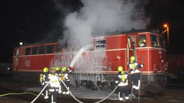 Feuerwehrleute löschen einen brennenden roten Zug mit Schaum.