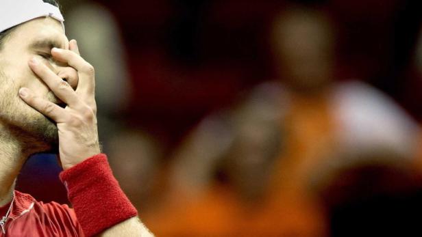 Ein Tennisspieler mit rotem Schweißband hält sich die Hand vor das Gesicht.