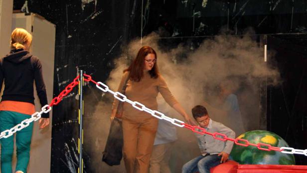 Auf einer Bühne interagieren Personen mit Requisiten und Ketten im Nebel.