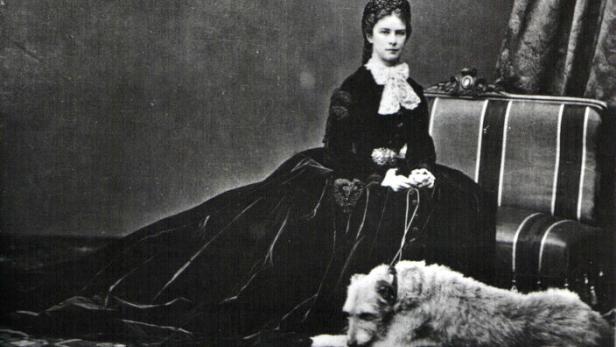 Kaiserin Elisabeth von Österreich sitzt mit ihrem Hund auf einem Sofa.