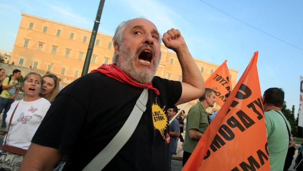 Ein Mann mit rotem Halstuch ruft auf einer Demonstration mit orangenen Fahnen.