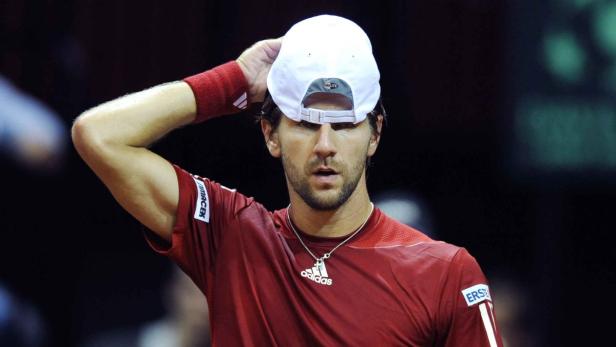 Ein Tennisspieler mit rotem Hemd und weißer Kappe kratzt sich am Kopf.