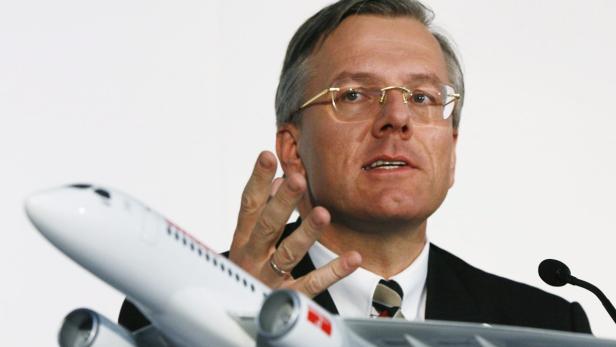 Ein Mann mit Brille gestikuliert neben einem Modellflugzeug.