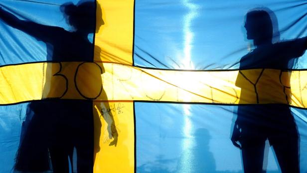 Die Silhouetten zweier Personen vor einer schwedischen Flagge mit der Aufschrift „30 BOY“.