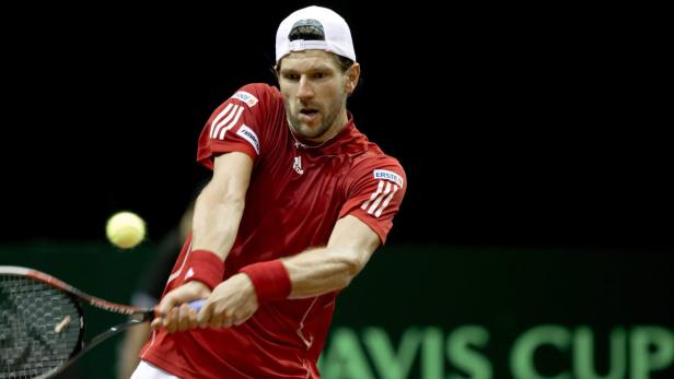 Ein Tennisspieler in rotem Hemd schlägt einen Ball.