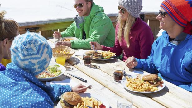 Eine Gruppe von Leuten isst Burger und Pommes an einem sonnigen Tag im Freien.