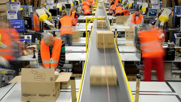 In einem Amazon-Logistikzentrum arbeiten Mitarbeiter an einem Förderband mit Paketen.