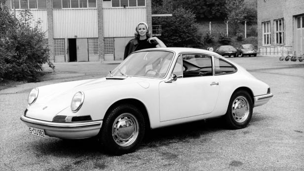 Eine Frau posiert an einem weißen Porsche 911 vor einem Gebäude.
