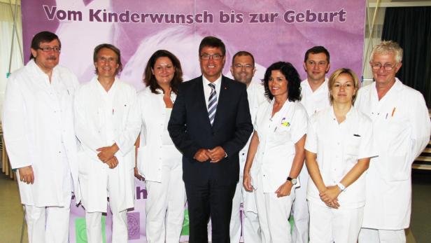 Eine Gruppe von Ärzten und medizinischem Personal posiert vor einem Banner mit der Aufschrift „Vom Kinderwunsch bis zur Geburt“.