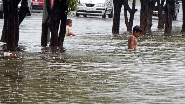 Zwei Jungen stehen im knietiefen Hochwasser auf einer überschwemmten Straße.