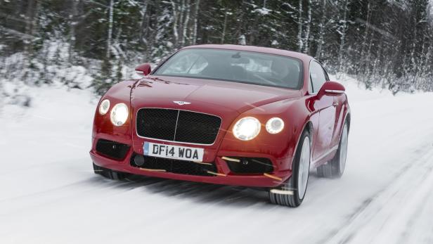 Ein roter Bentley fährt auf einer schneebedeckten Straße durch einen winterlichen Wald.