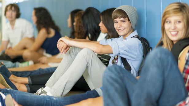 Eine Gruppe von Teenagern sitzt an einer blauen Wand in einem Flur.